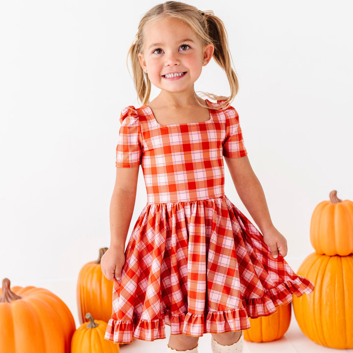 little girl wearing pink and orange plaid twirl dress with square neckline