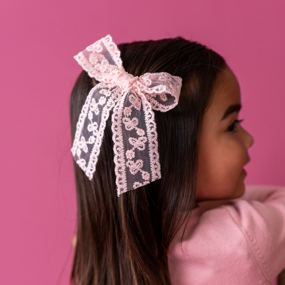young girl in pink sweater and matching light pink lace bow on clip