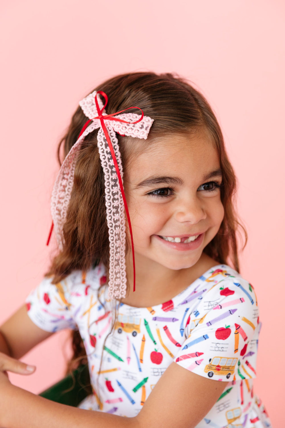 little girl in school themed twirl dress and matching pink lace long tailed bow with red ribbon overlay