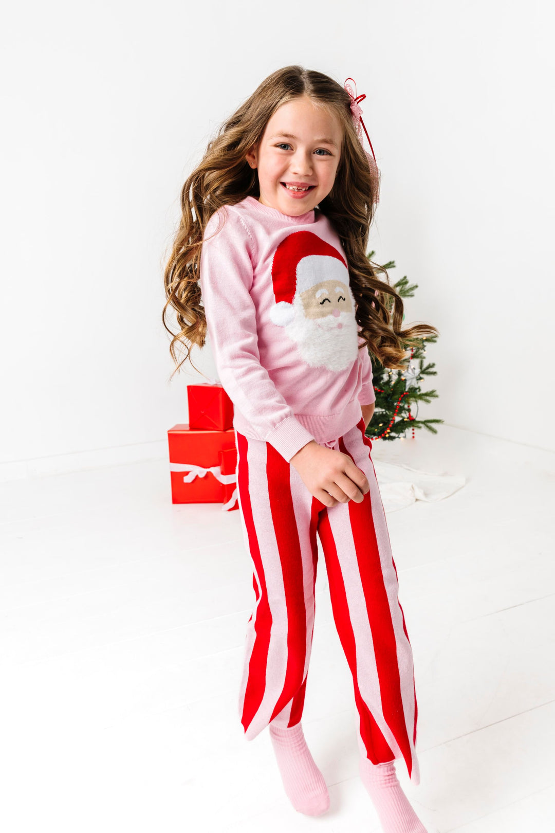 little girl in front of Christmas tree in pink cotton knit sweater with fluffy Santa design and matching pink and red seater pants