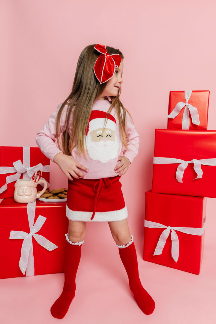 little girl in pink Santa sweater with coordinating bow, socks and sweater skirt in re with white trim