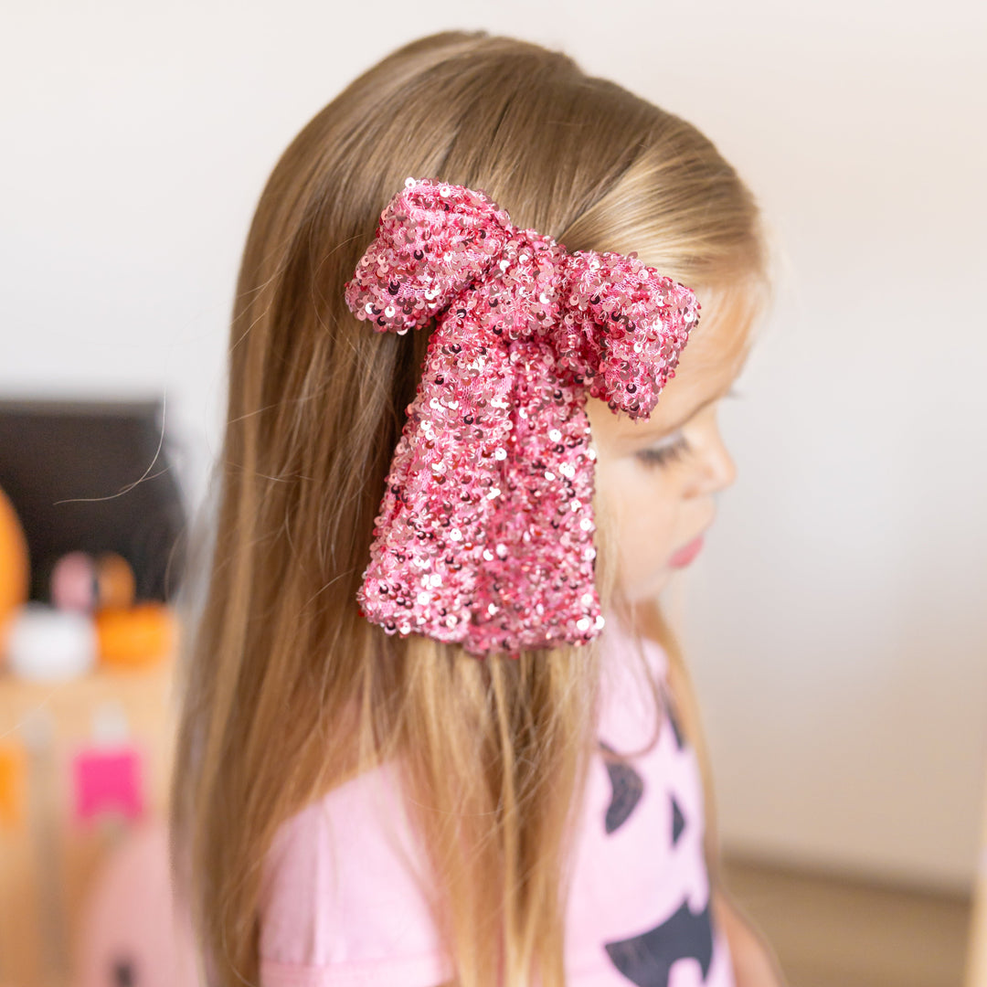 little girl in pink oversized bow with sequins and matching pink tee with jack-o-lantern design