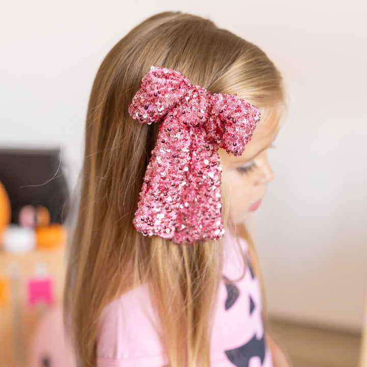 little girl in pink oversized bow with sequins and matching pink tee with jack-o-lantern design