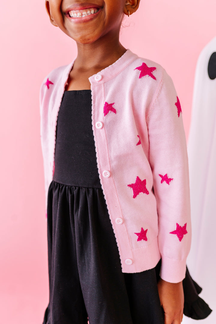 young girl in black cotton blend twirl dress paired with light pink cardigan with hot pink sparkle knit star design for Halloween