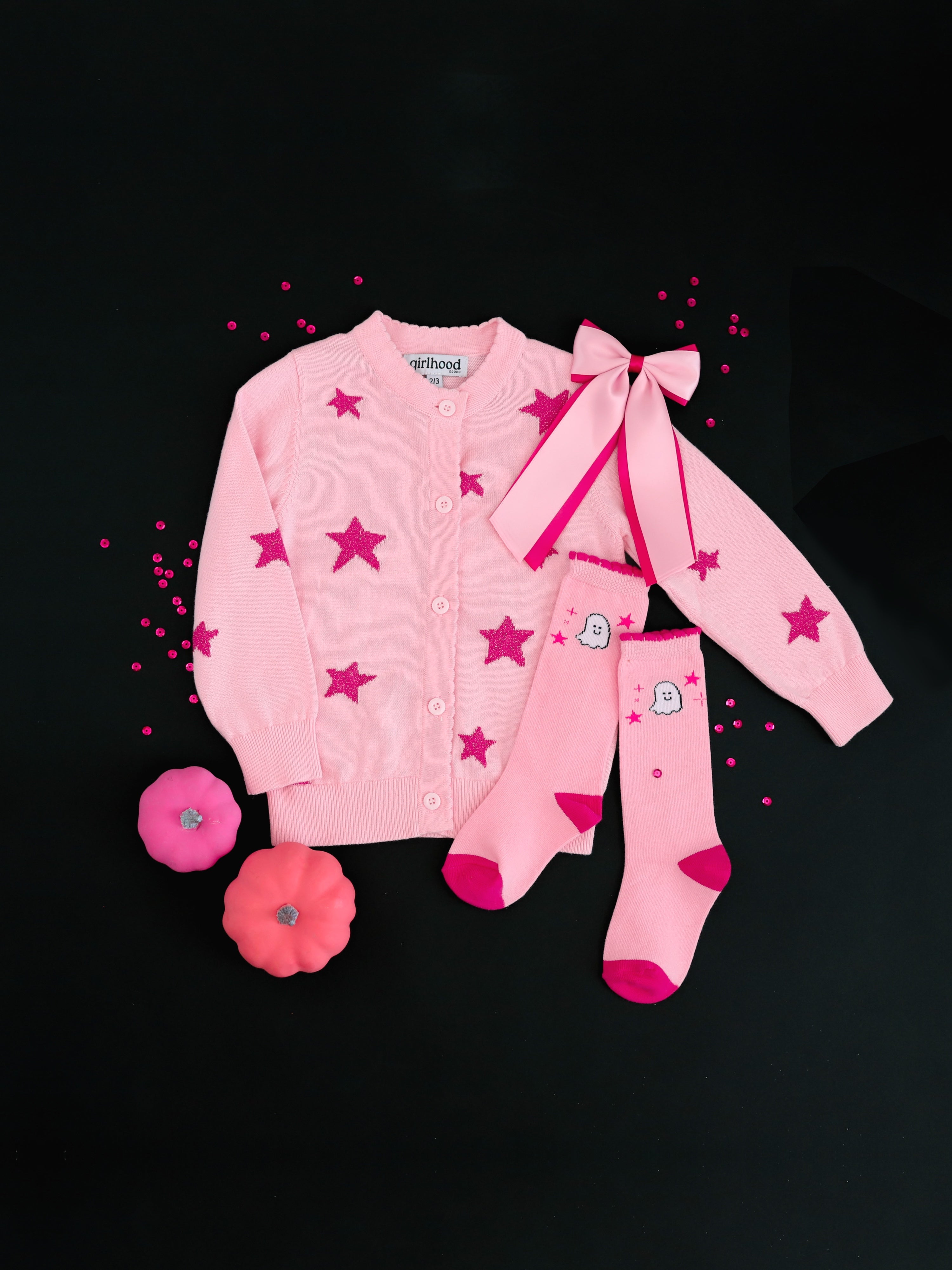 girls' light pink cotton knit cardigan with pink sparkle yarn stars paired with matching pink ghost and star print knee socks, two-tone pink satin layered bow photographed on black background with pink confetti and pumpkins