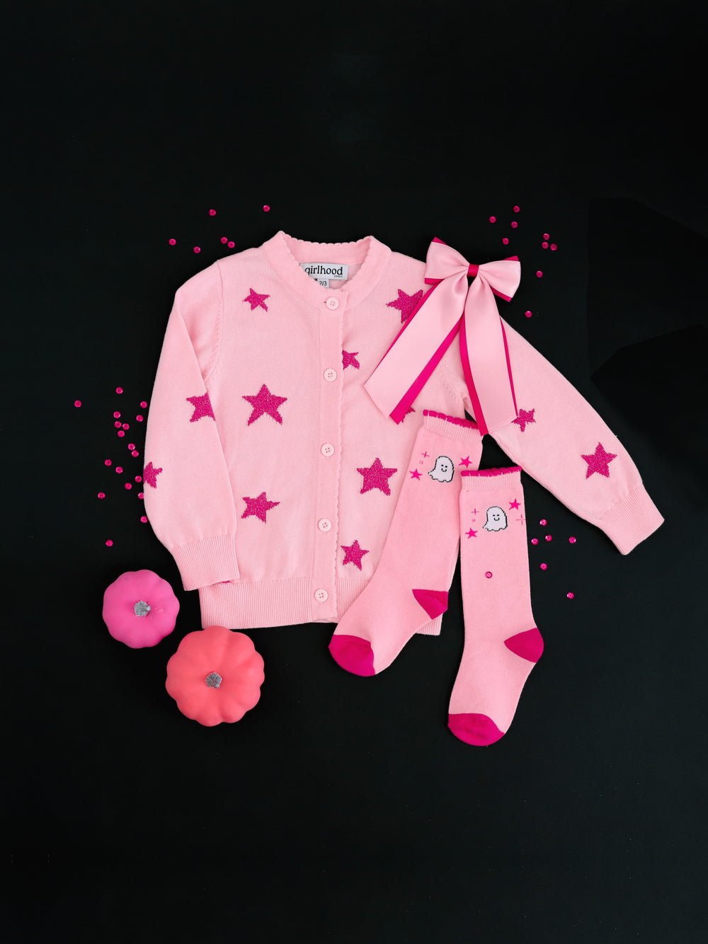 girls' light pink cotton knit cardigan with pink sparkle yarn stars paired with matching pink ghost and star print knee socks, two-tone pink satin layered bow photographed on black background with pink confetti and pumpkins