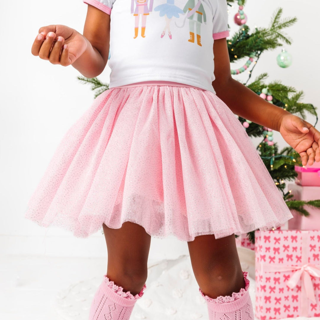 little girl by Christmas tree in sparkly light pink tulle tutu skirt and nutcracker print top 