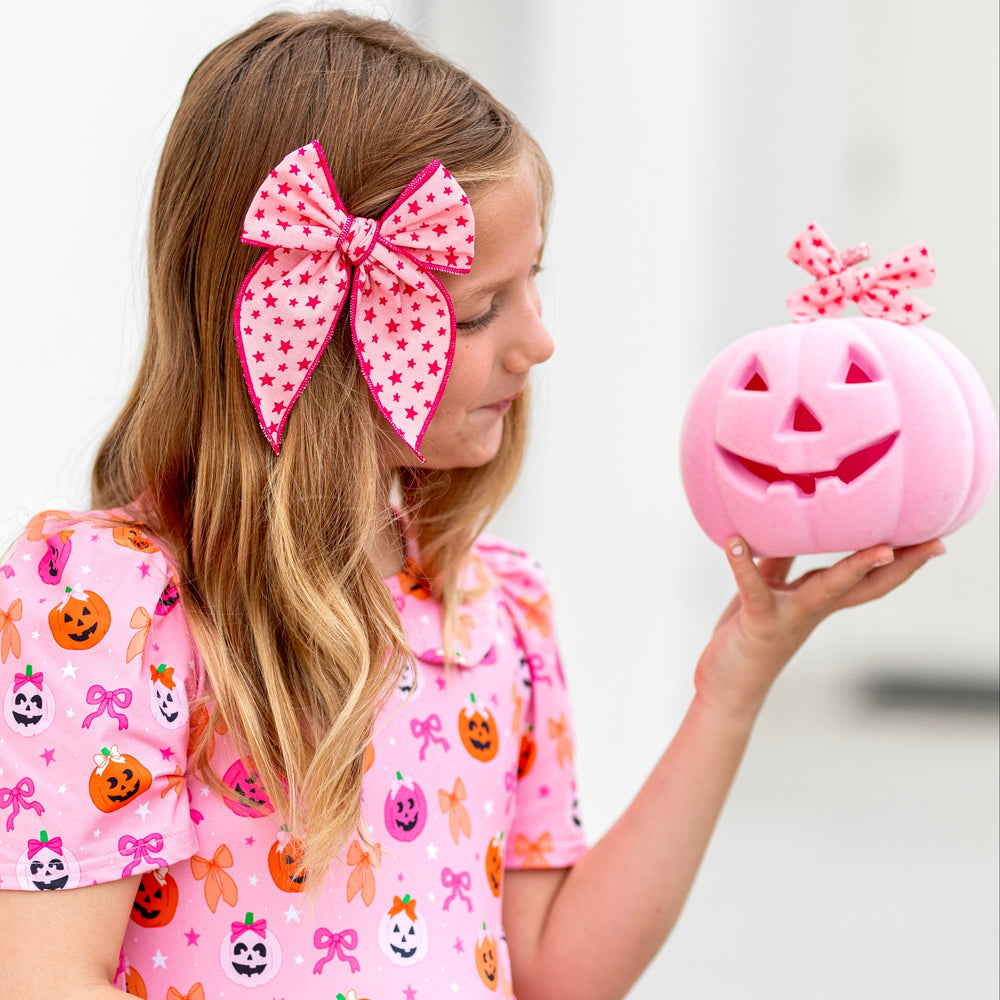 girl holding pink pumpkin in pink fabric bow with dark pink trim and star print paired with pink Halloween pumpkin print twirl dress