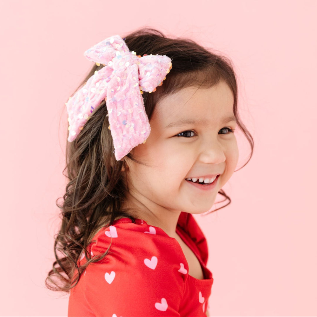 little girl in pink velvet and sequin bow on clip and matching red twirl dress with pink heart print