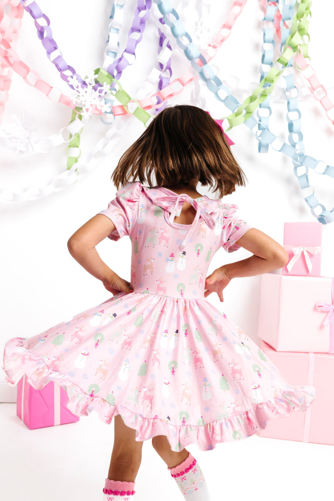 girl twirling in front of winter wonderland decor in pastel pink twirl dress with winter themed Christmas print