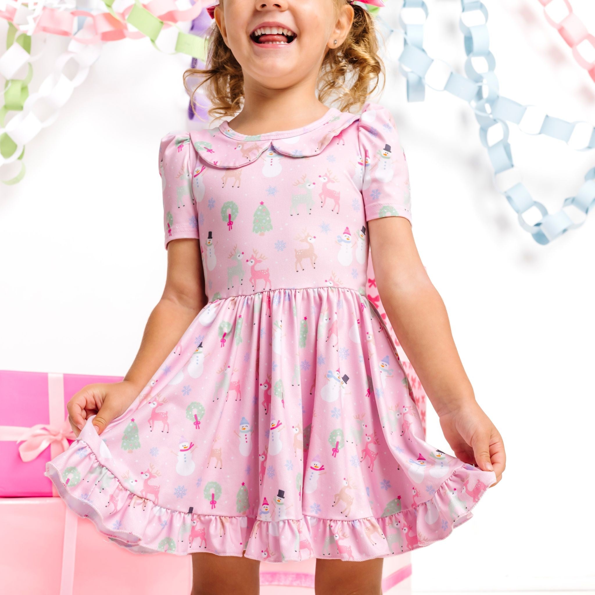 little girl wearing light pink, short sleeve, collared Christmas twirl dress with pastel winter themed print