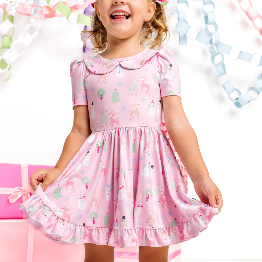 little girl wearing light pink, short sleeve, collared Christmas twirl dress with pastel winter themed print