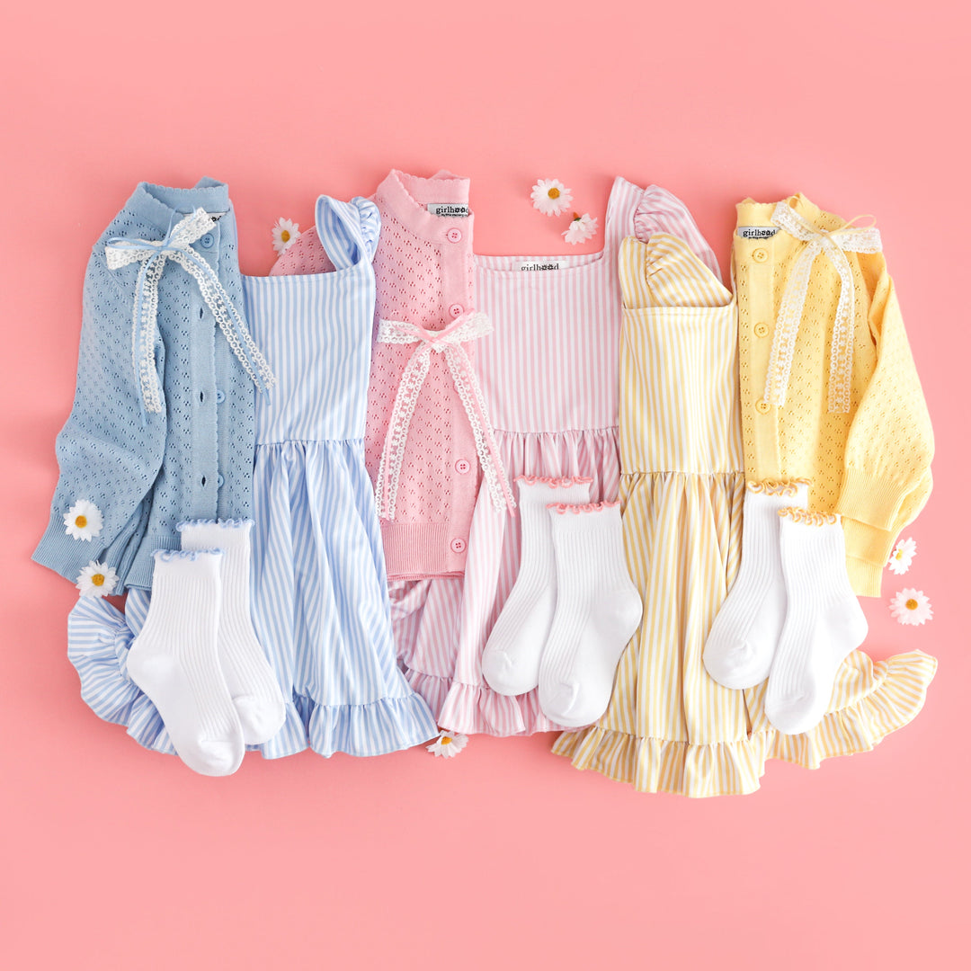 Collection of children's clothing including dresses and cardigans on a pink background