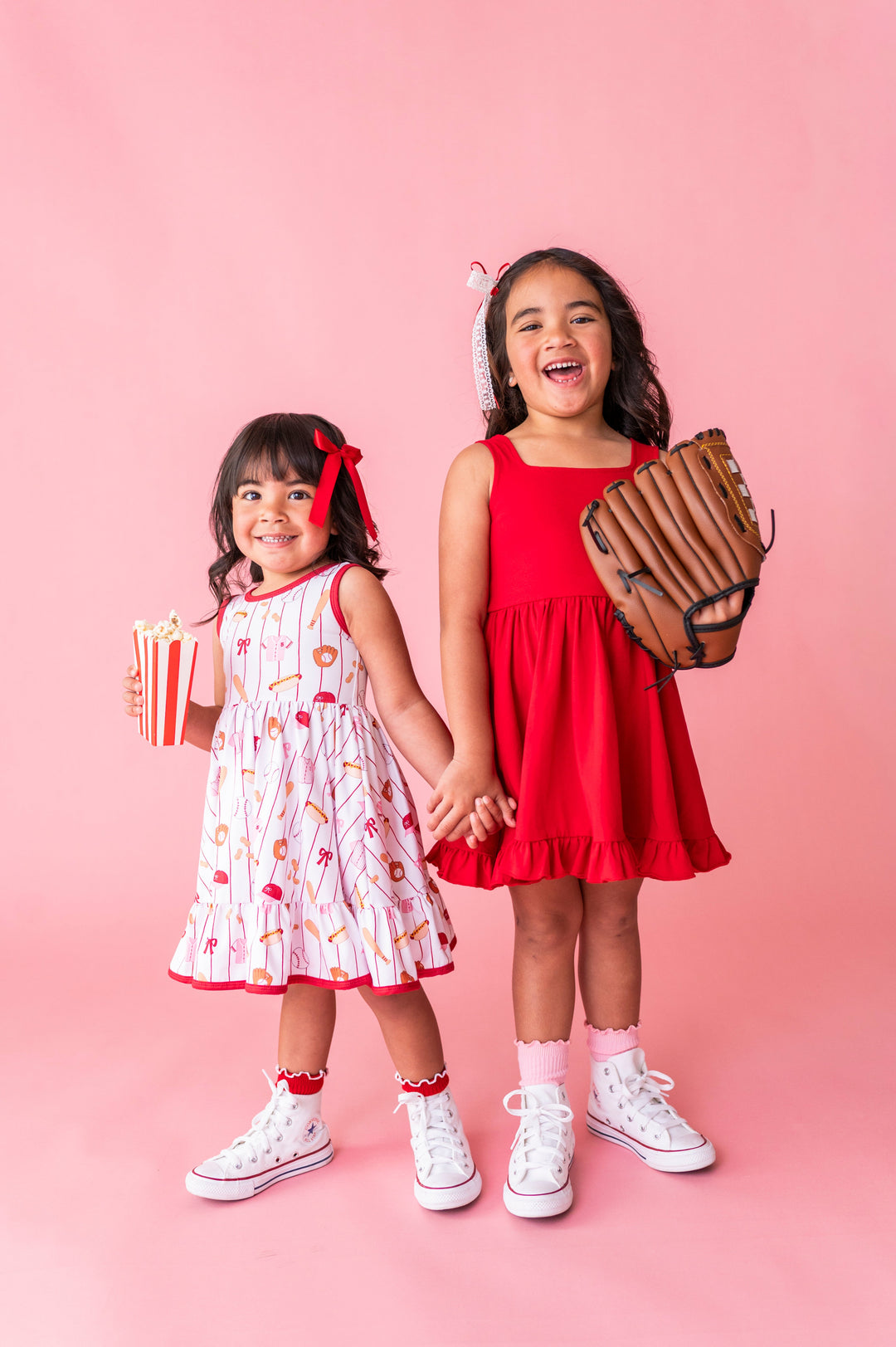 sisters in coordinating baseball print and bright red twirl dresses styled for a summer baseball game