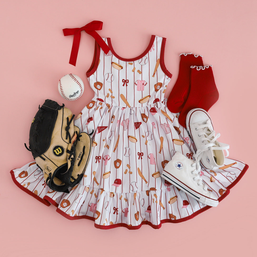 girls' baseball print sleeveless twirl dress in shades of red, white and pink styled with glove, ball and matching red accessories