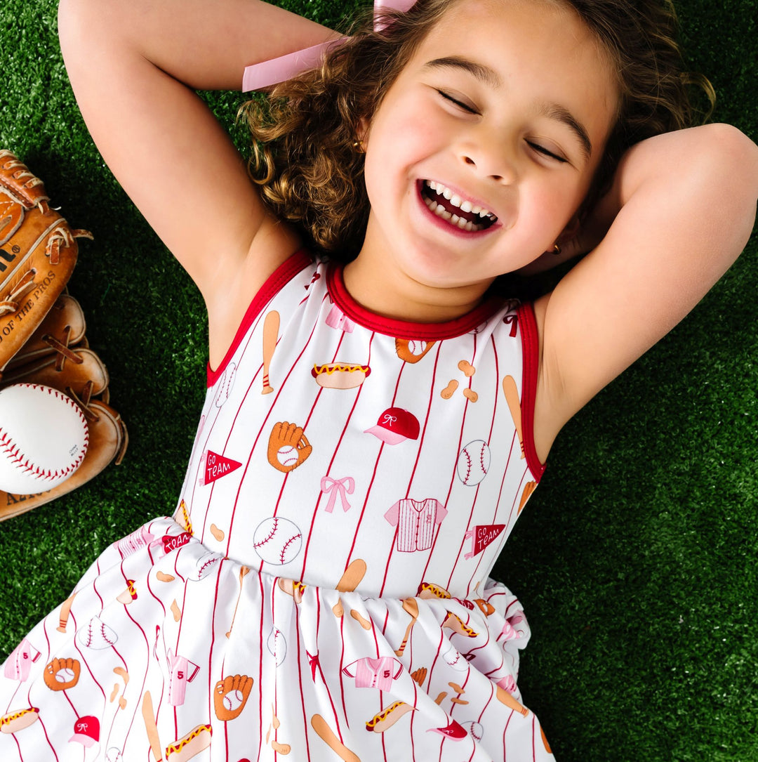 little girl laying in grass in baseball print sleeveless summer dress