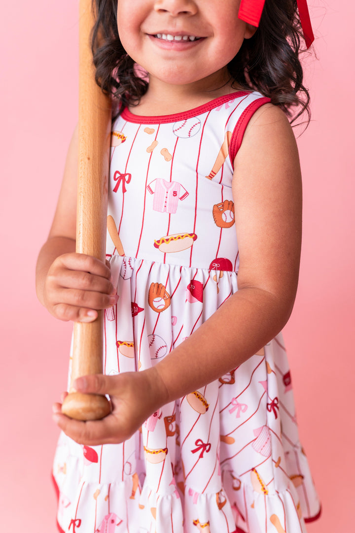 closeup of little girl in baseball print twirl dress on white with red and pink details 