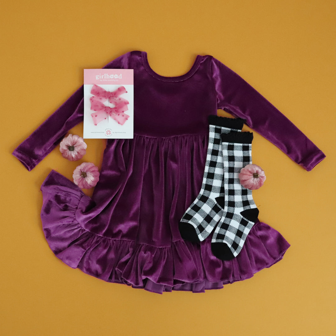 girls deep purple long sleeve velvet twirl dress with ruffle styled for fall with buffalo plaid print knee-high socks and sheer pink pigtail bows