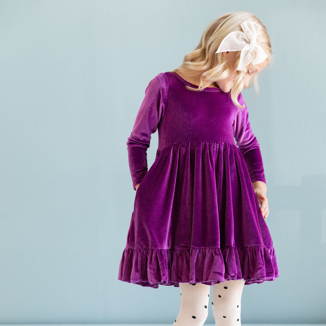 little girl in long sleeve purple velvet twirl dress with cream velvet bow and matching polka dot tights