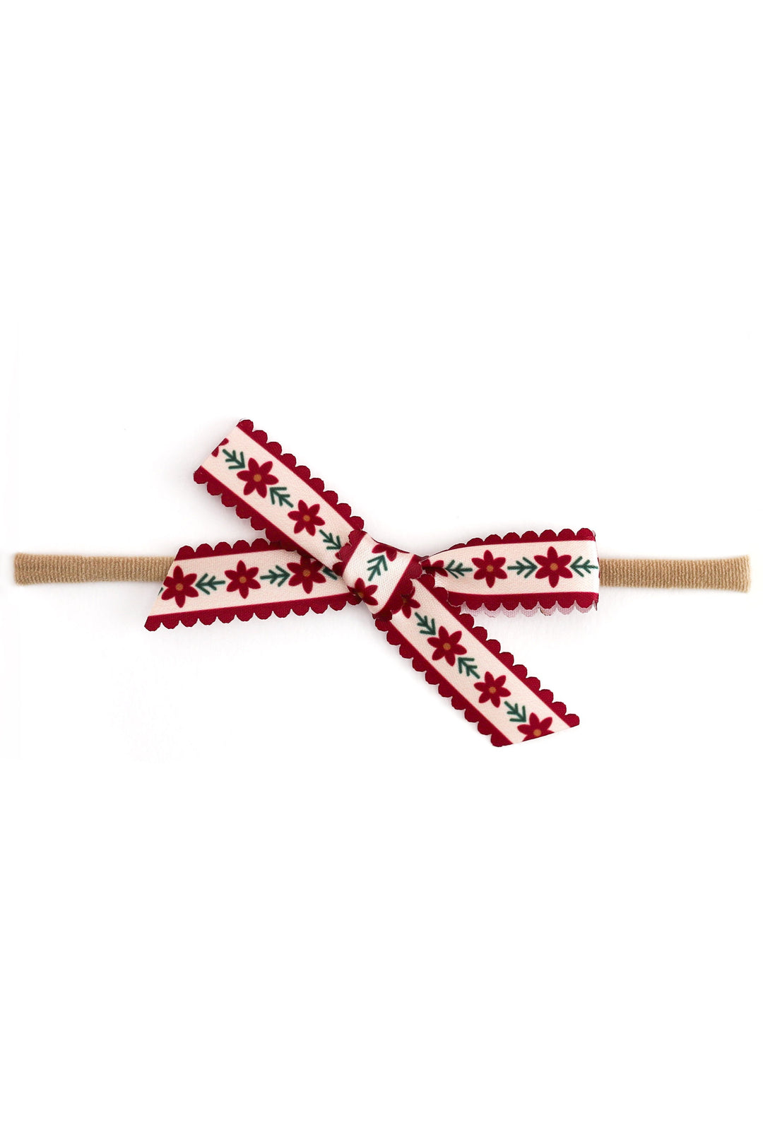 A festive baby headband featuring a nylon elastic tan band and a decorative bow made from a vanilla ribbon with red scalloped edges, red poinsettia motifs, and green leafy accents.