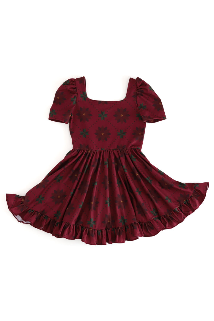 A dark red short-sleeve dress with a square neckline, puff sleeves, and a ruffled hem, decorated with a dark green poinsettia floral pattern, shown against a plain white background.