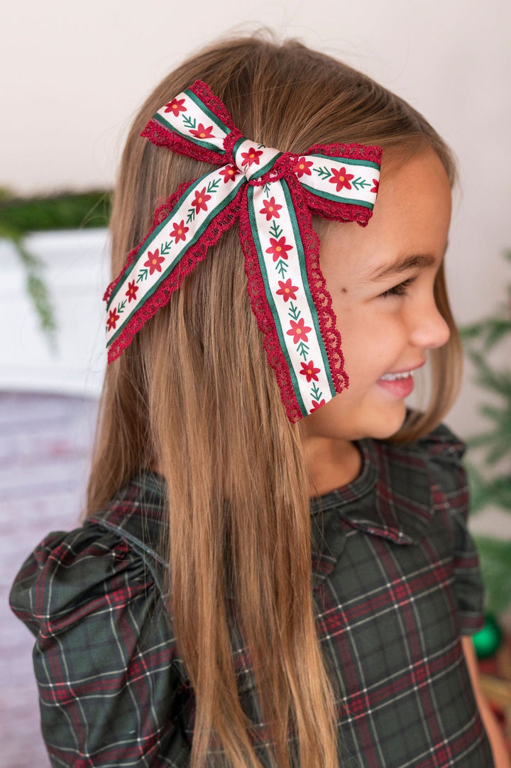little girl in plaid xmas dress wearing poinsettia printed ribbon bow with deep crimson red lace