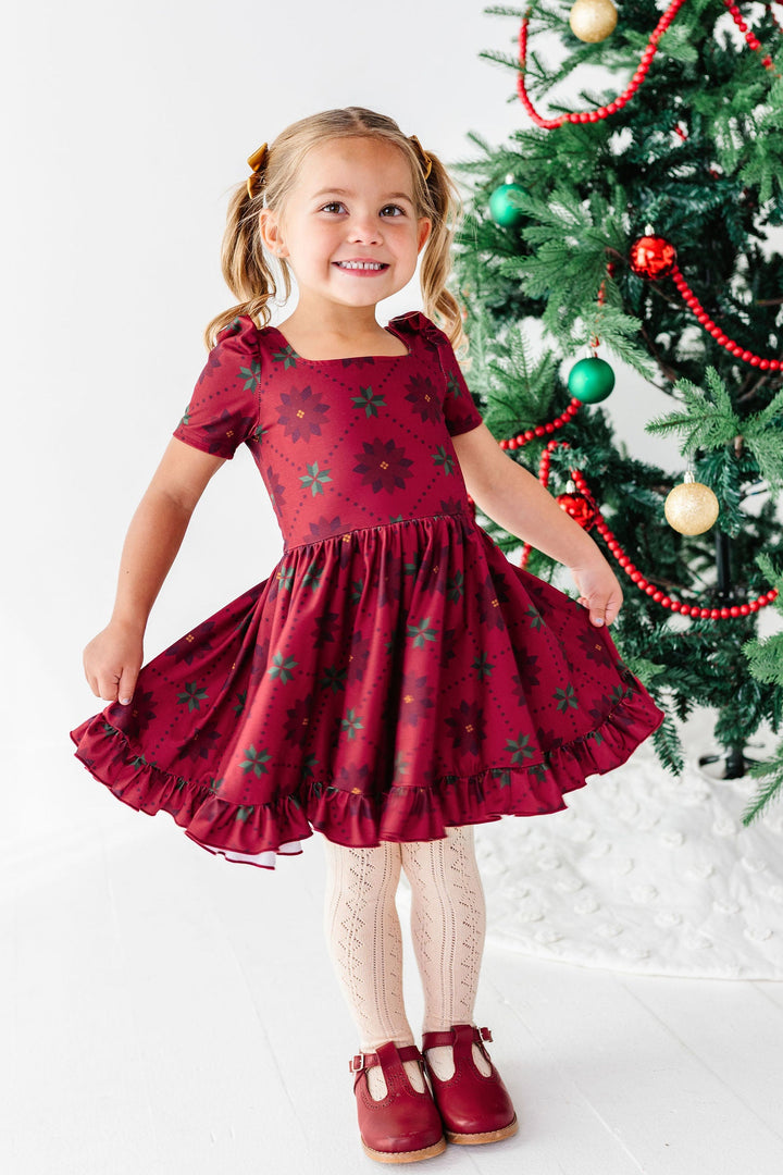 girl standing in front of christmas tree wearing red poinsettia print christmas dress