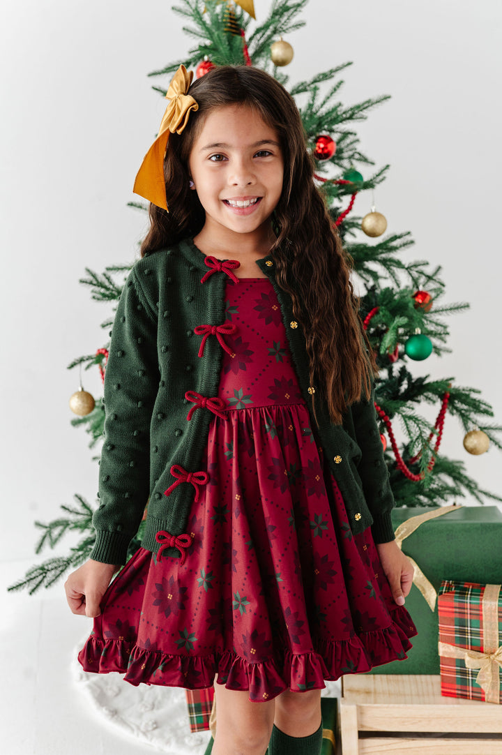 girl wearing crimson red poinsettia print dress with matching forest green cardigan