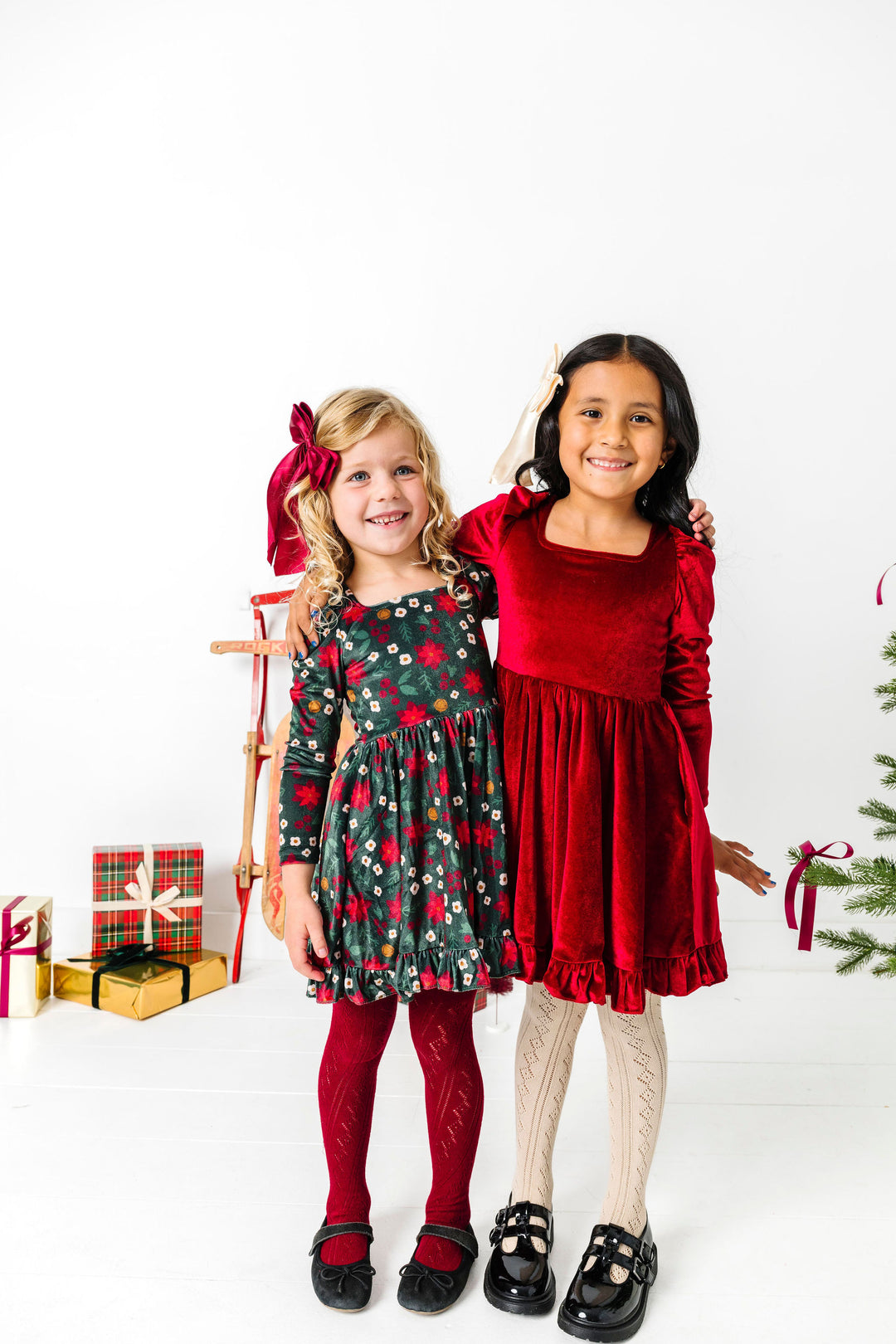 two girls in long sleeve Christmas velvet twirl dresses with coordinating open knit tights and satin bows