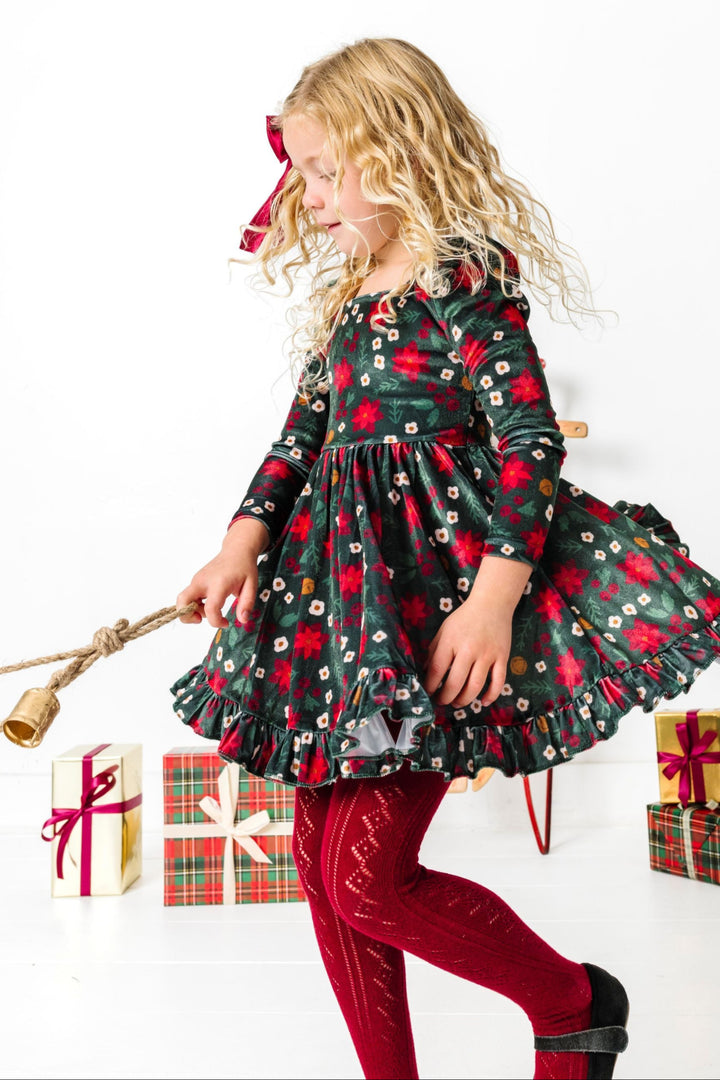 little girl twirling with Christmas bell wearing forest green and crimson velvet poinsettia print dress and matching crimson open knit tights