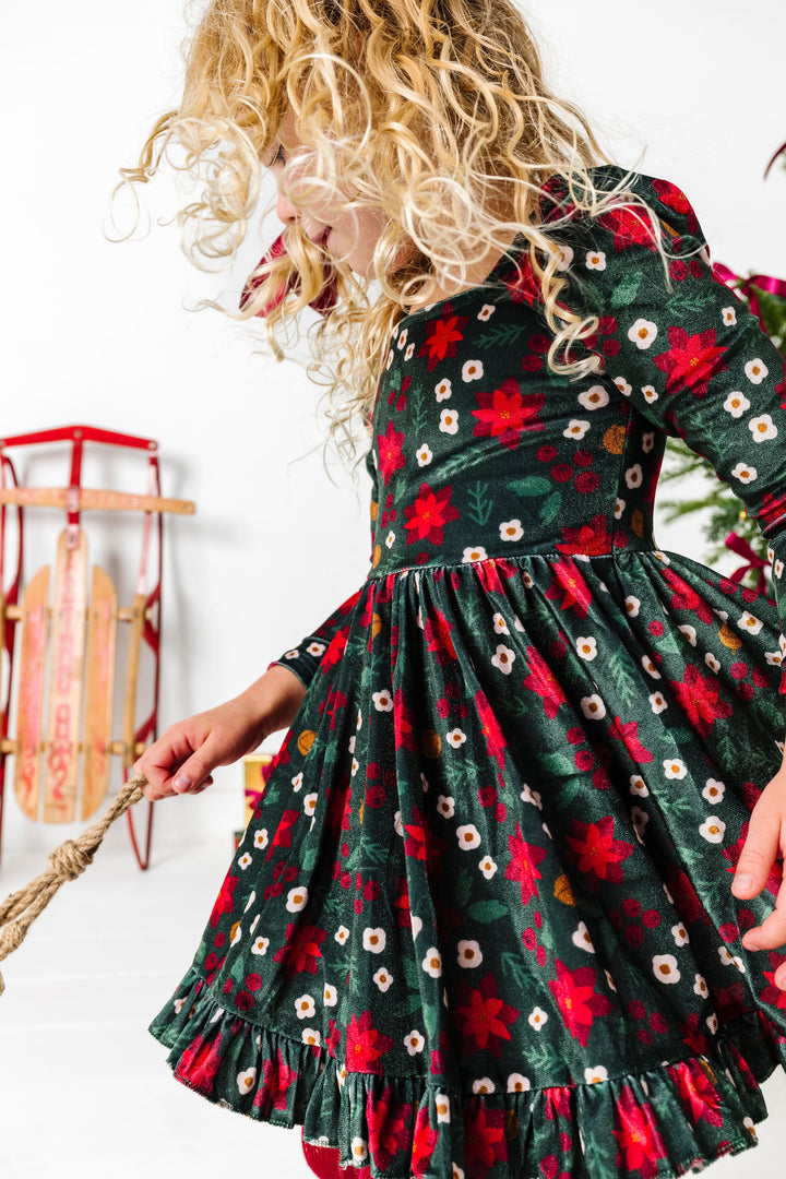 close up of girl twirling in deep green velvet dress with poinsettia print for Christmas Eve