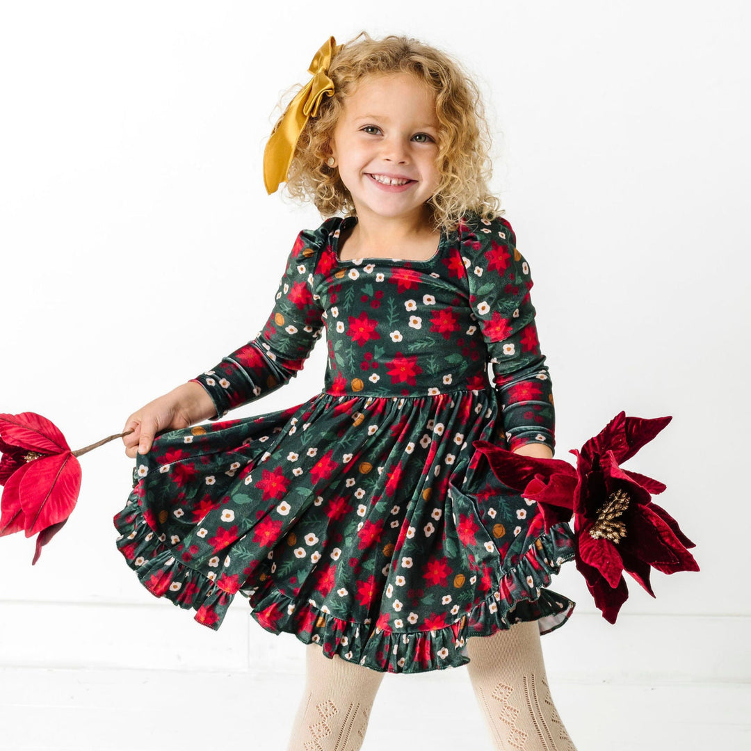 little girl holding poinsettias in green velvet long sleeve twirl dress with poinsettia print, gold satin bow and open knit cream tights for Christmas party