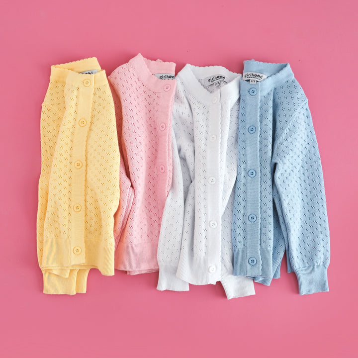 flat lay of four cotton knit pointelle cardigans to match girls' spring collection of dresses in pastel yellow, pink, white and blue