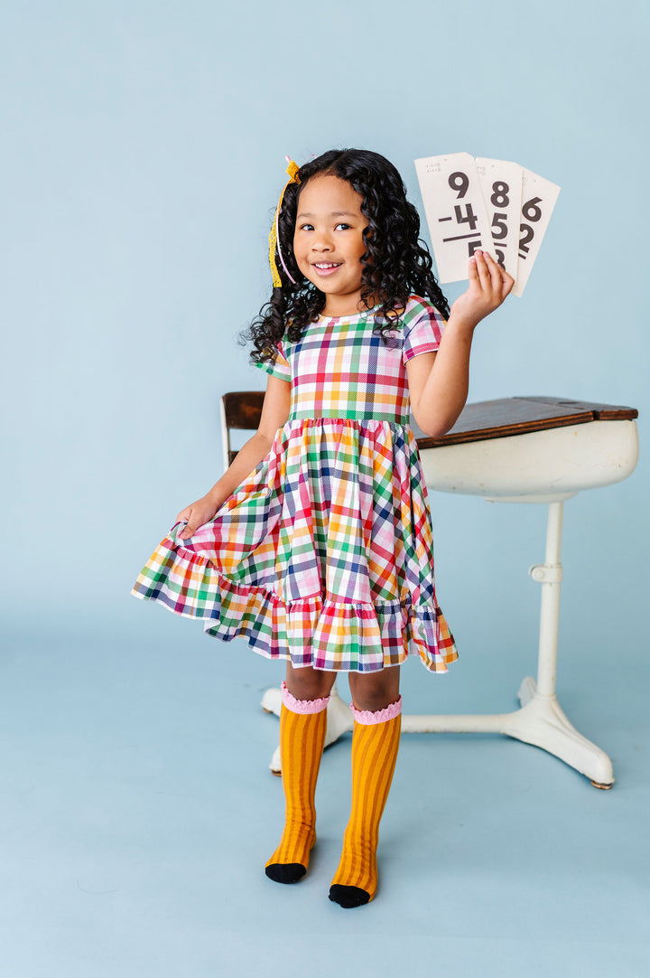 girl holding math flash cards in white with primary color gingham print twirl dress paired with pencil socks and matching lace ribbon bow