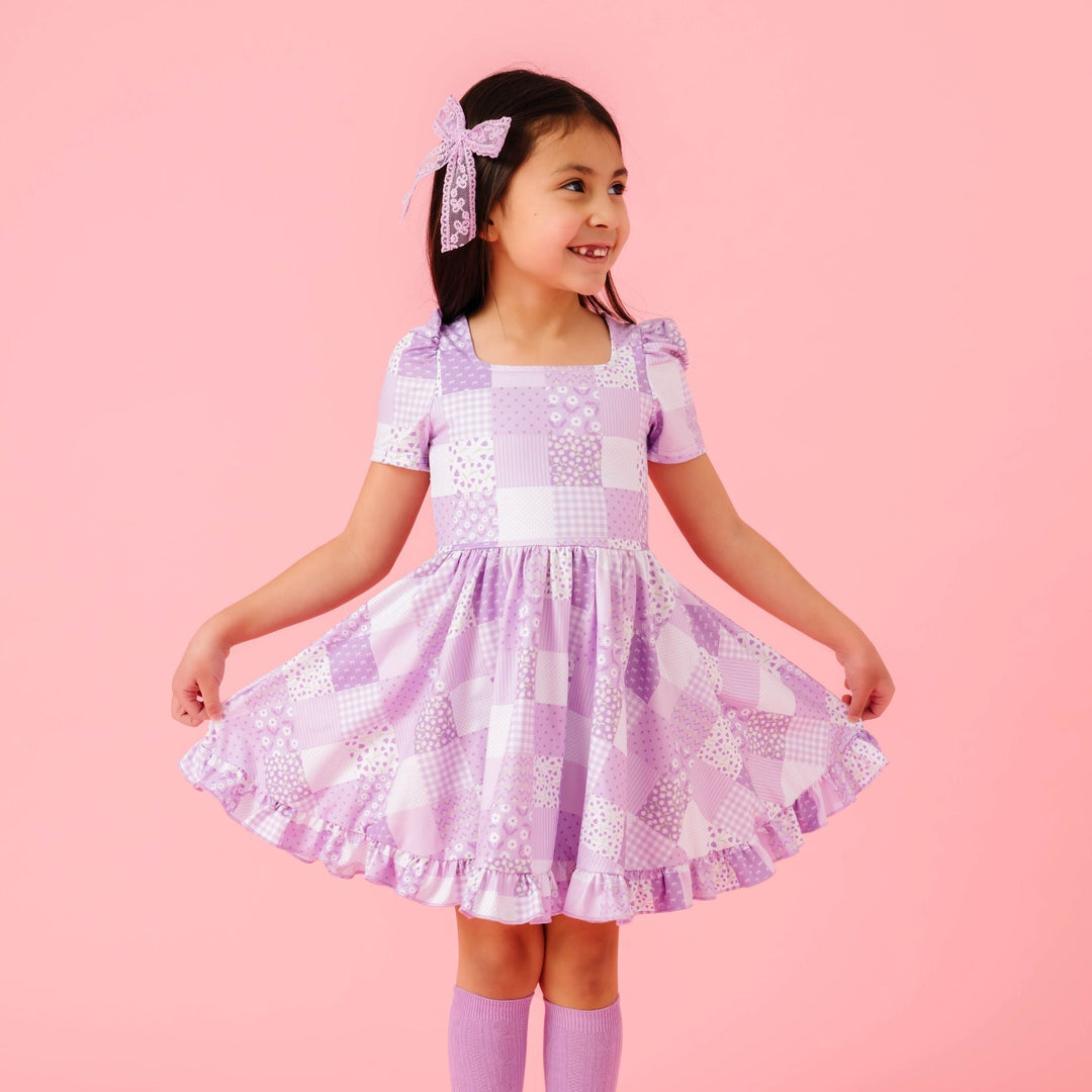 little girl in floral pattered patchwork twirl dress in shades of purple with matching light purple accessories