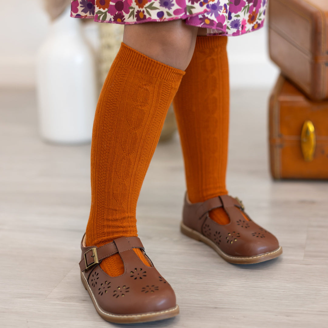 closeup of little girl in brown mary janes with pumpkin spice cable knit knee highs paired with fall floral skort 