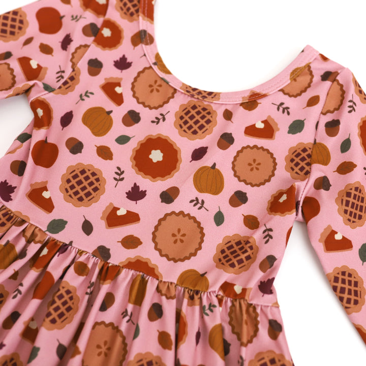 closeup of girls long sleeve printed twirl dress with fall leaves, acorns, pumpkin and apple pie