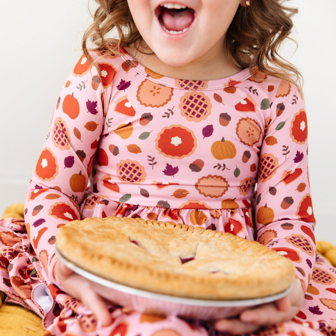 little girl holding pie in a long sleeve pumpkin pie print dress for Thanksgiving