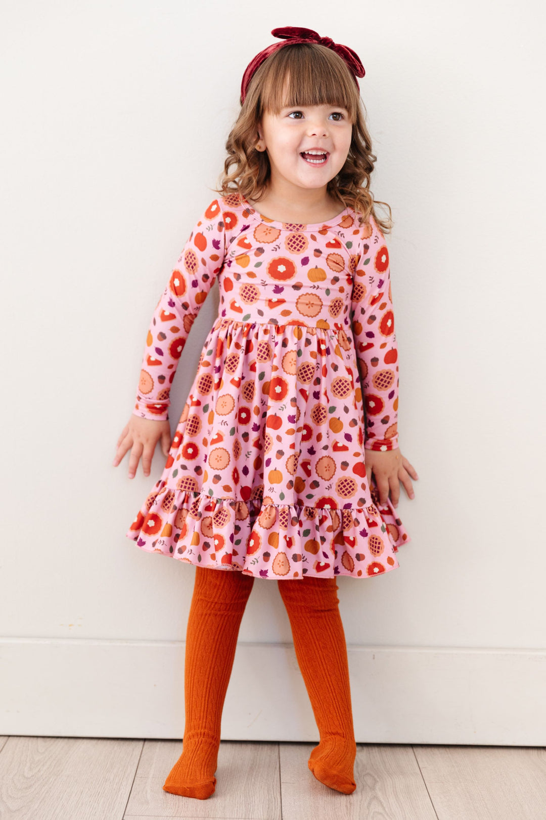 little girl in pink Thanksgiving pie dress with matching orange cable knit tights and burgundy velvet headband