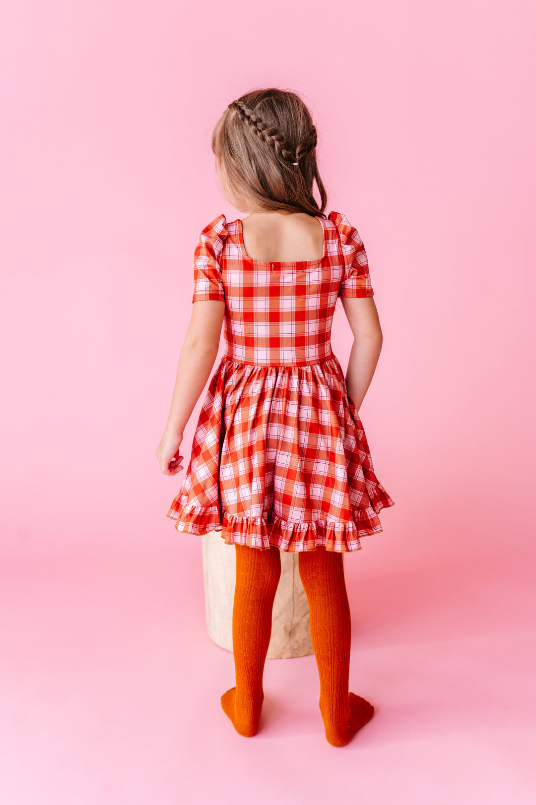 little girl showing back view of square neck design on orange plaid twirl dress paired with matching orange cable knit tights