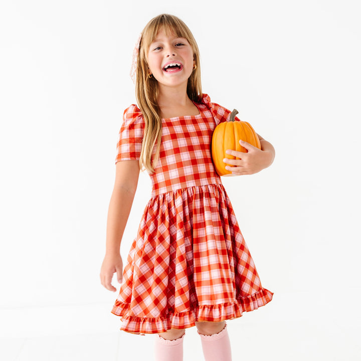 little girl holding pumpkin in orange and light pink plaid twirl dress with square neck and short sleeves for fall