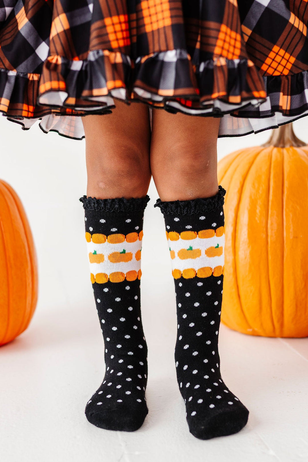 girl wearing halloween outfit with pumpkin knee high socks and matching plaid dress