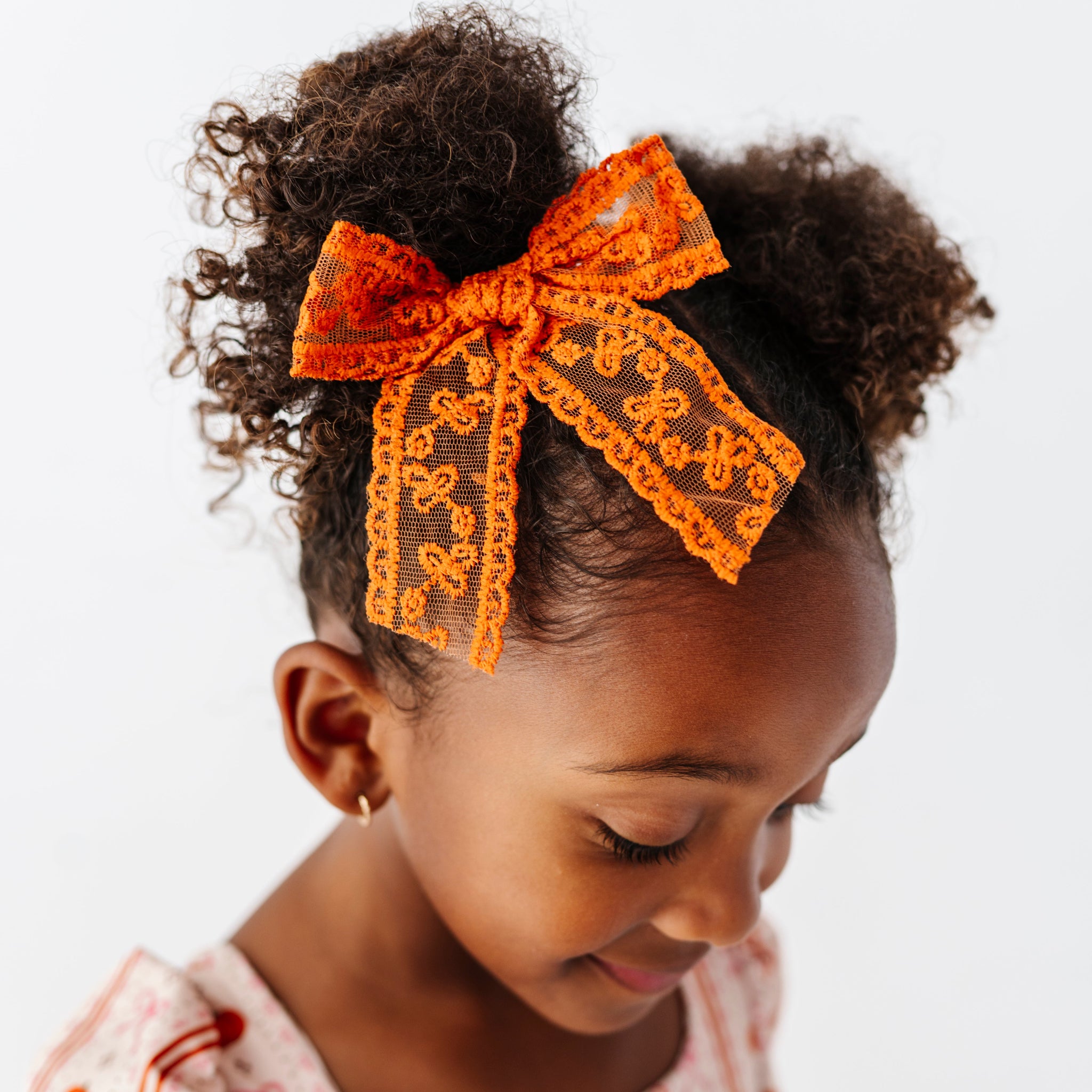 young girl in pigtails and Thanksgiving pumpkin dress paired with orange lace hair bow on clip