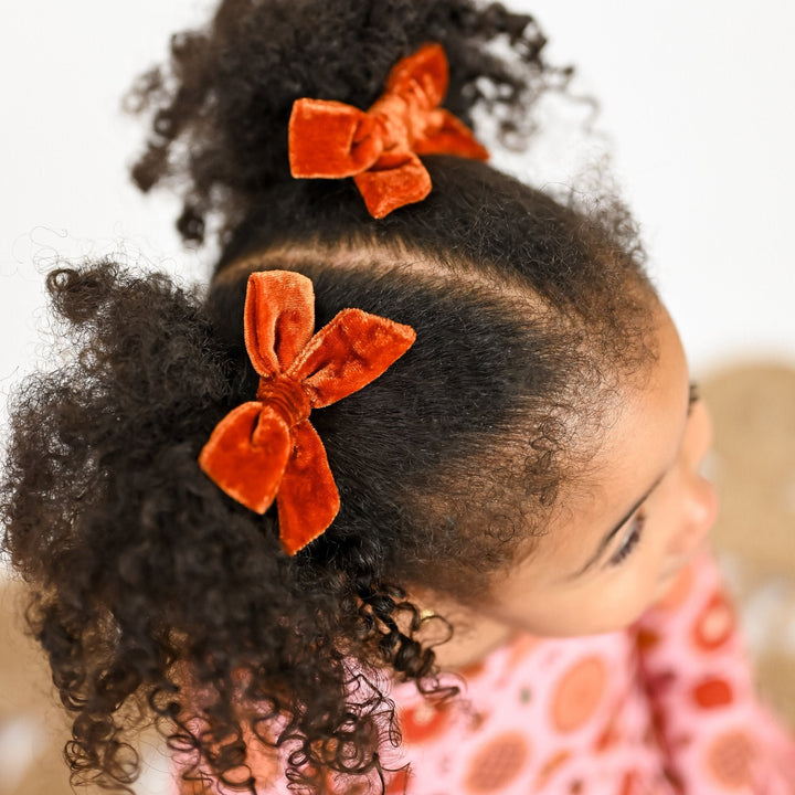 little girl in orange fall velvet pigtail clips and matching pumpkin pie dress for Thanksgiving