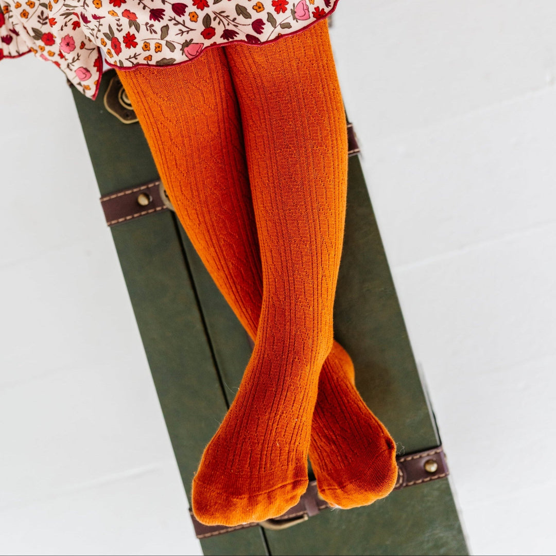 young girl sitting on green vintage suitcase in burnt orange cable knit tights and coordinating fall floral twirl dress