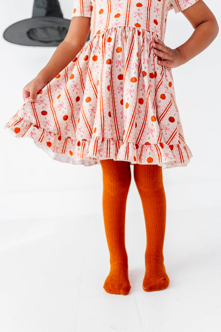 little girl in cream pumpkin wallpaper twirl dress paired with matching orange cable knit tights