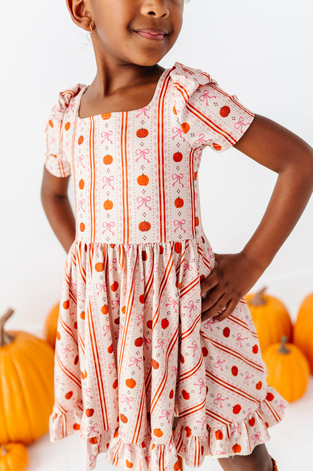 closeup of little girl in front of pumpkin sweater cream vintage pumpkin and bow wallpaper print twirl dress 