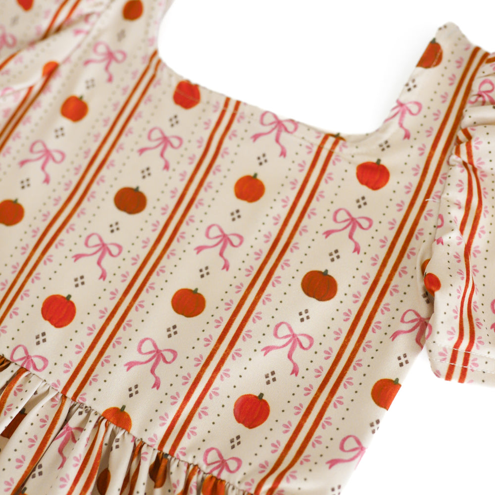 close up of girls' cream dress bodice with orange pumpkins and pink bows in a wallpaper inspired pattern