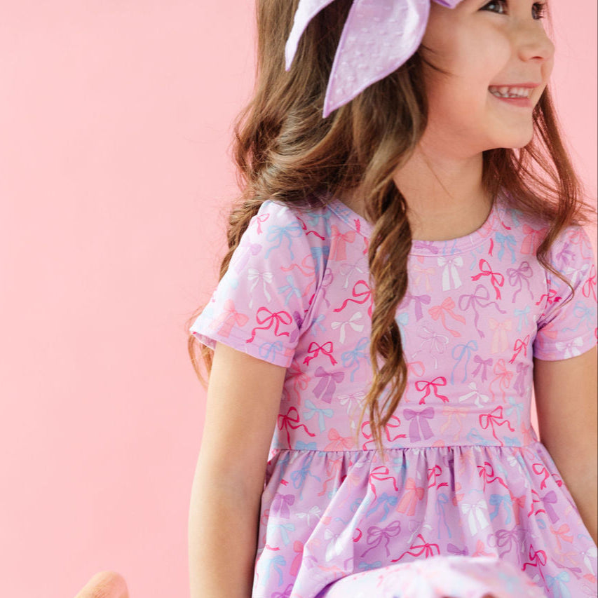 girl wearing purple dress with pink, purple, white and blue bow pattern