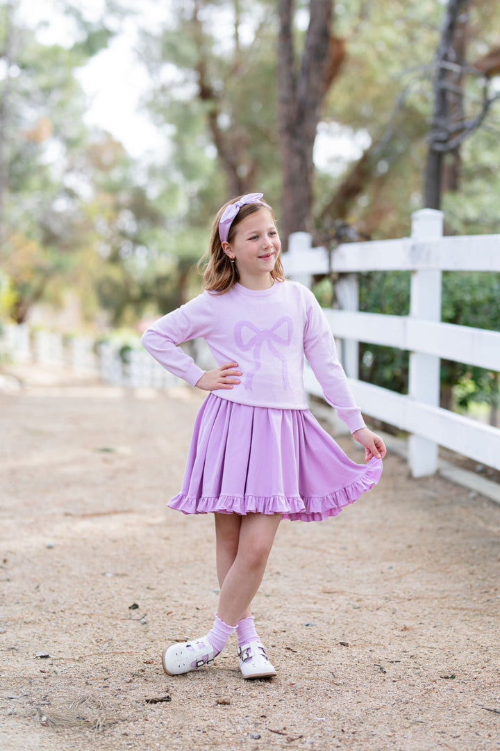 girl in two tone purple sweater with bow design and matching purple dress and accessories for spring